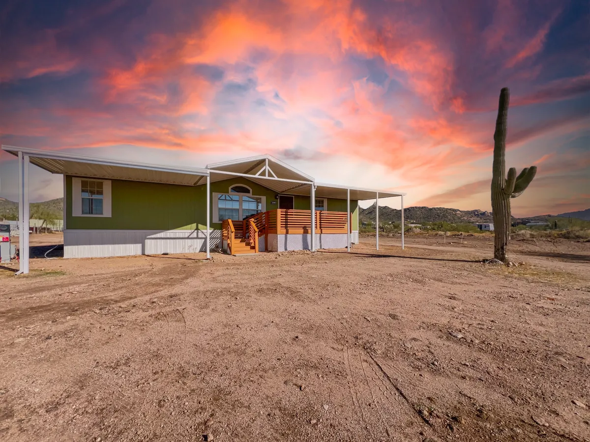 The photo showcases the green exterior of the home, a wooden deck, cactus in the foreground, and a richly colored sky. The vantage point hints at tranquil outdoor gatherings, stargazing, and the ease of access to the surrounding natural environment.