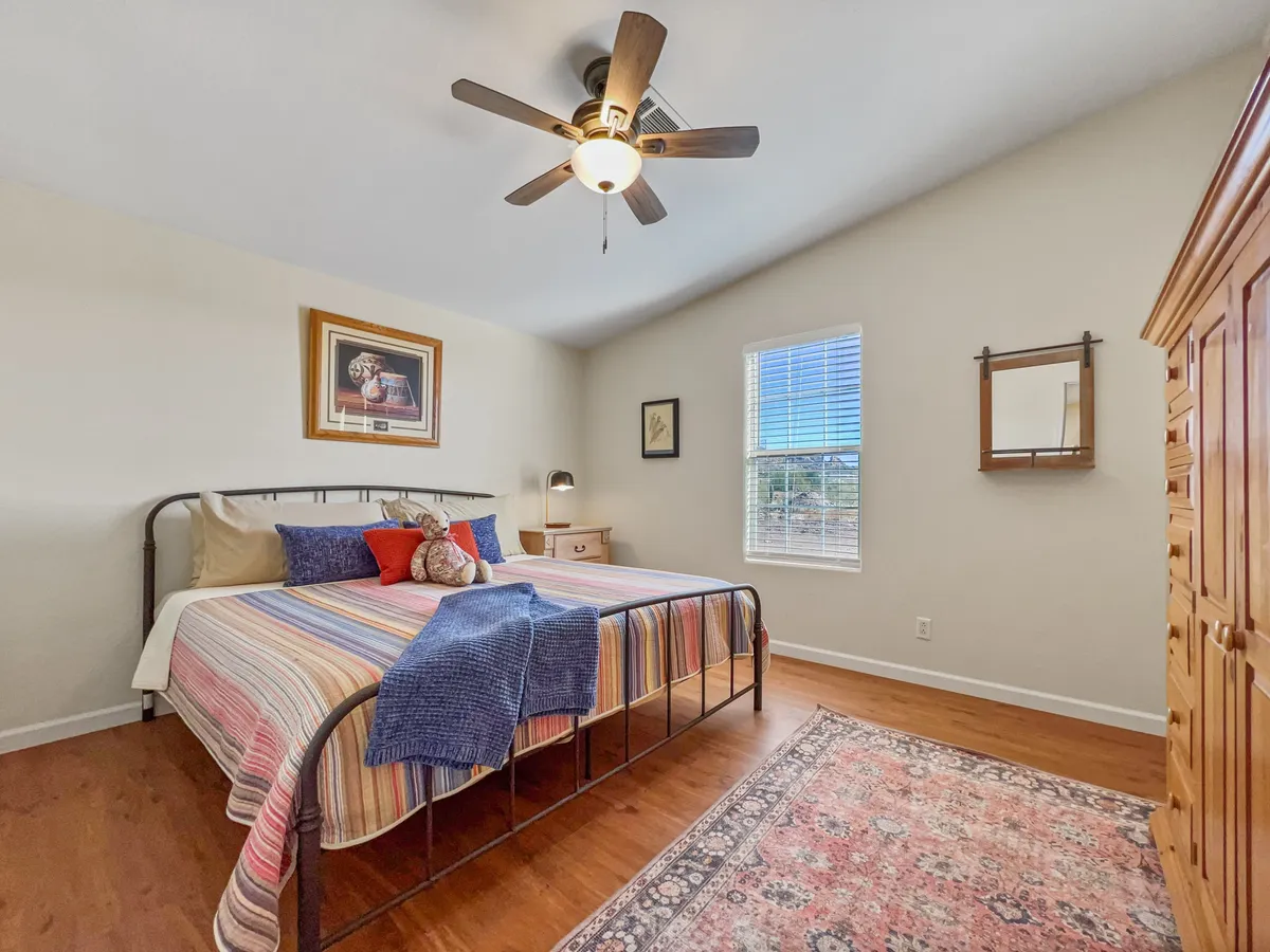 A cozy bedroom with a bed adorned in colorful bedding, framed artwork above the bed, and a wooden dresser. Soft natural light fills the room, creating a tranquil and restful atmosphere.