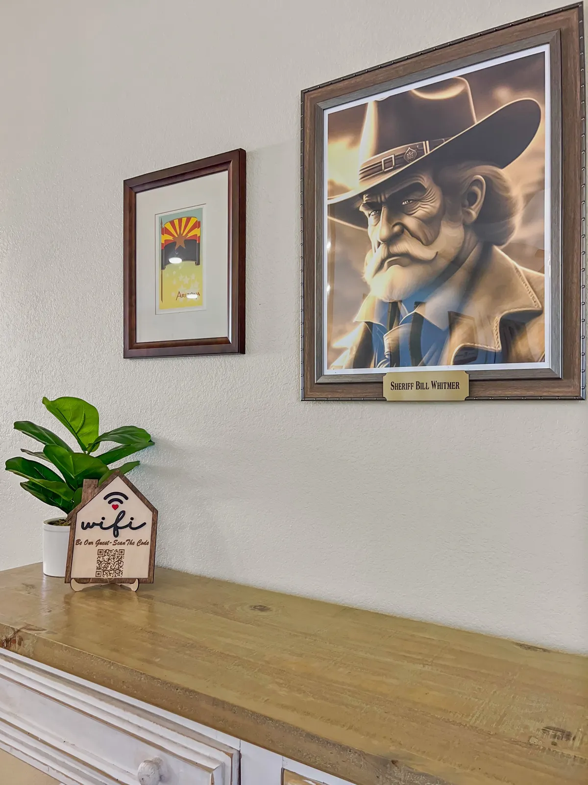 This image features a cozy corner of the interior, accented by a portrait of Sheriff Bill Whitmer, Arizona-themed artwork, a visible WiFi sign, and a lush potted plant. The scene is styled to be welcoming and hints at both the historical and regional flavor of the property, while the WiFi sign subtly signals modern connectivity.