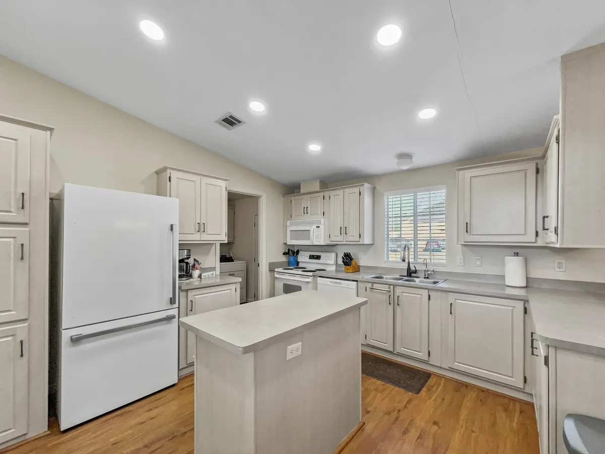 A practical, functional kitchen view featuring a well-equipped island, white refrigerator, cabinetry, sink, and a sunlit window. The layout emphasizes ample prep space and essential amenities, making meal preparation a breeze.