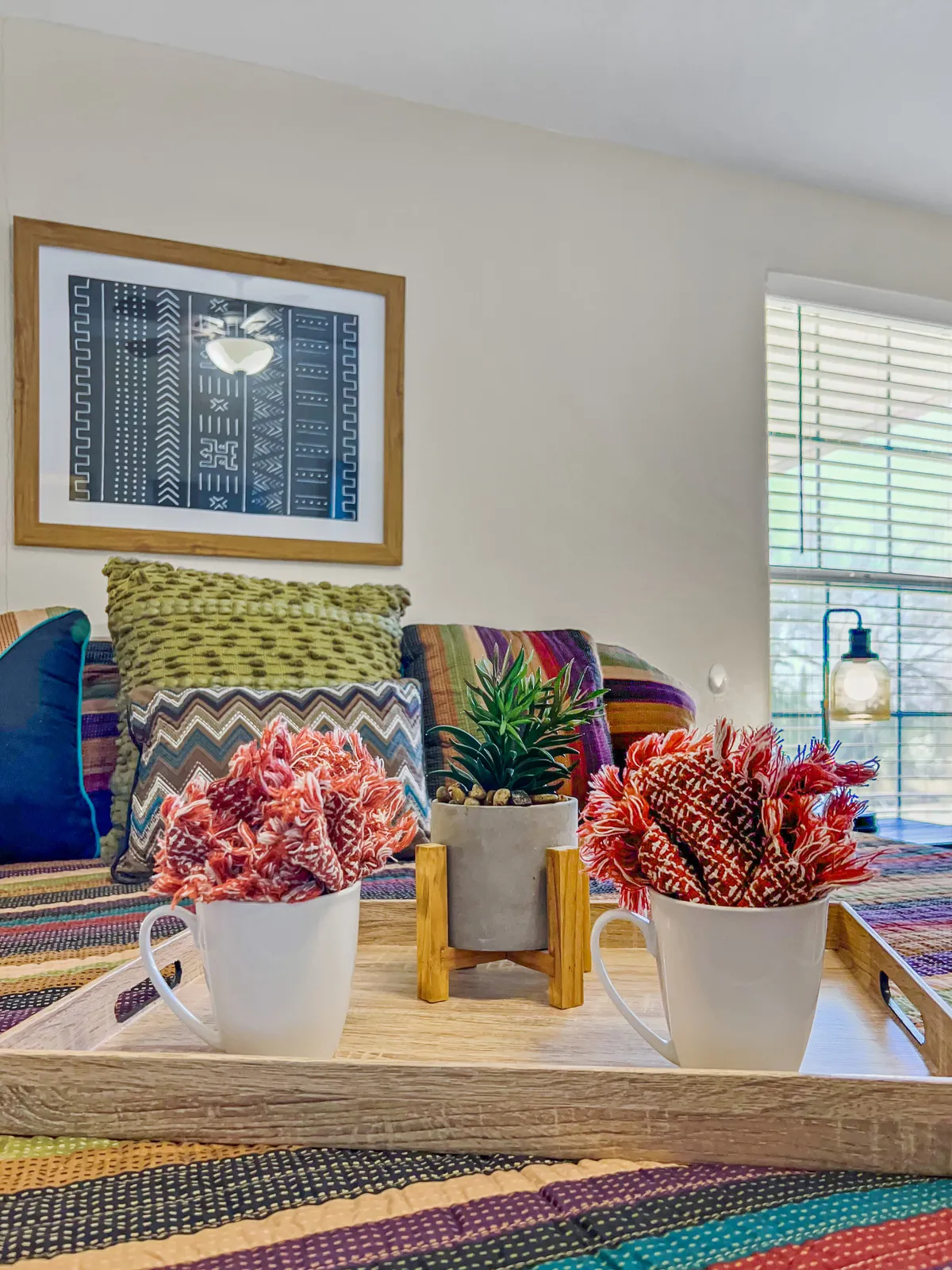 A close-up of decorative cups filled with flowers, a small potted plant, textured pillows, and framed wall art, all arranged atop a table. The scene suggests moments of relaxation paired with artistic touches, reinforcing a sense of comfort and creativity.