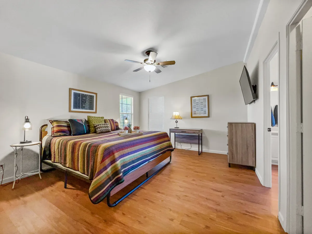 A cozy bedroom with striped bedding, warm ambient lighting from lamps, decorative artwork, and wooden furniture. The space feels intimate and inviting, embodying a tranquil hideaway vibe that's perfect for couples.