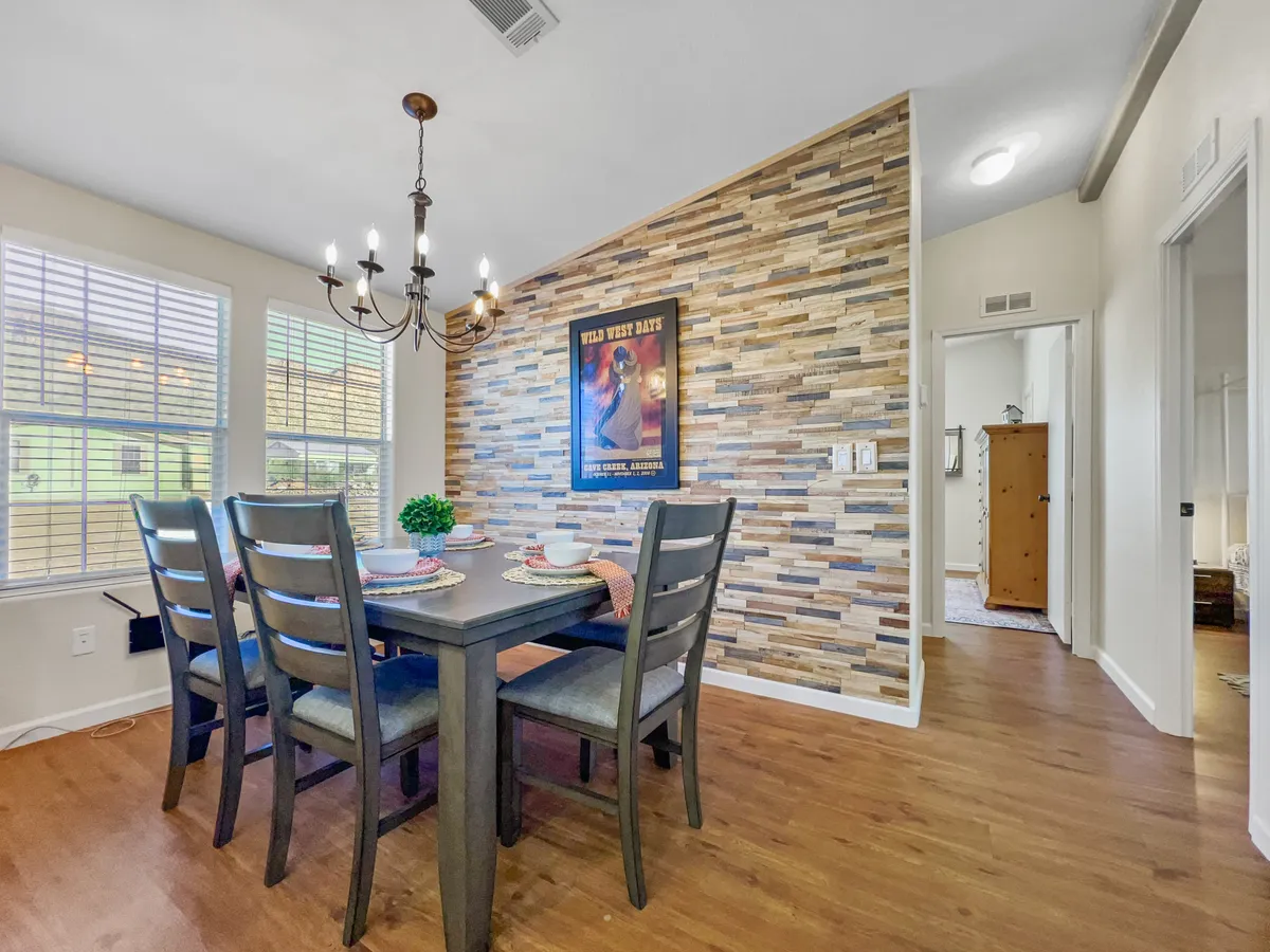 The dining area is showcased with a large table under a stylish chandelier, surrounded by decorative wall art and textured walls. The ambiance is warm and inviting—perfect for family dinners, celebrating special occasions, or planning the next day's adventure.