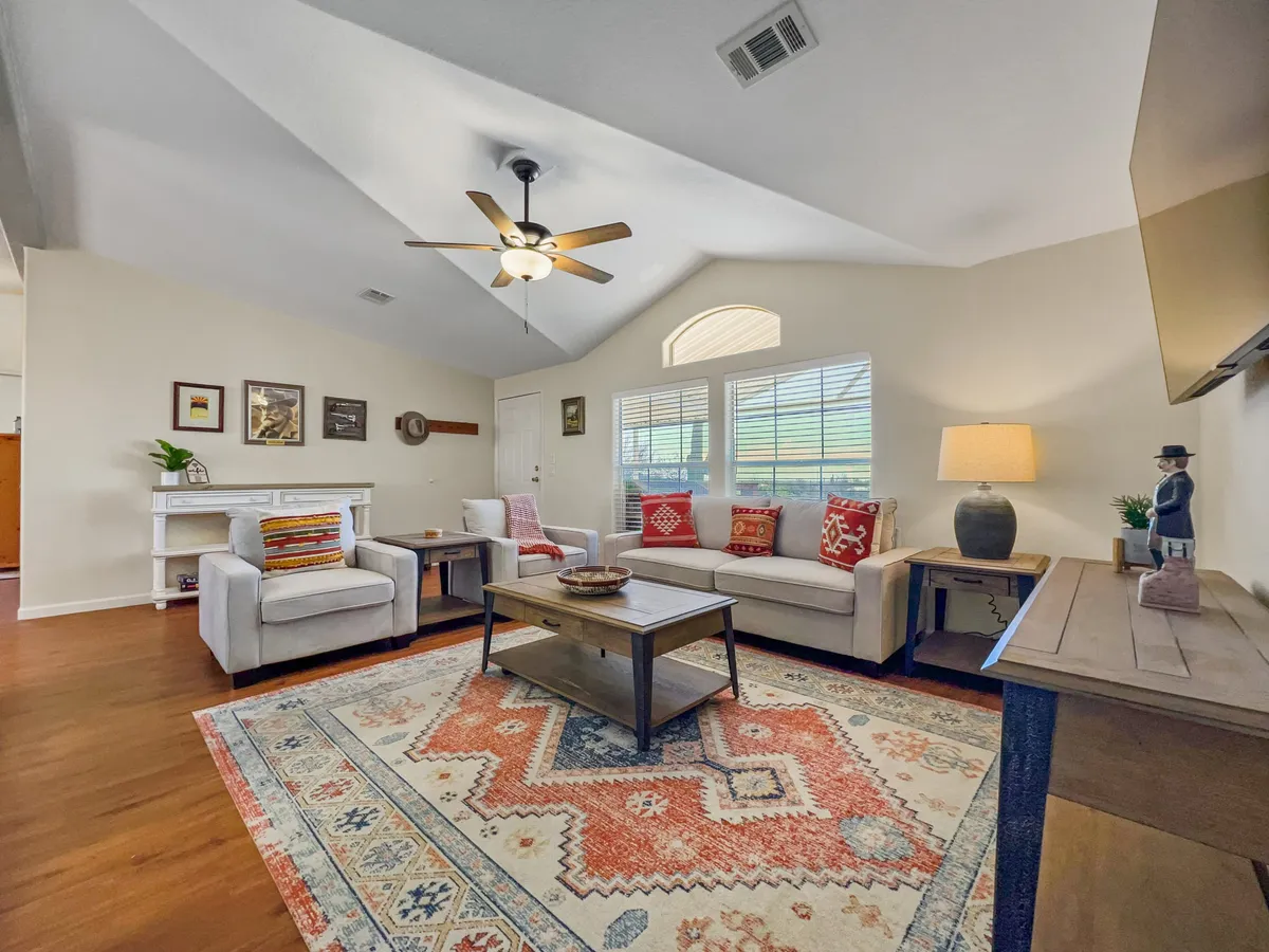 This image features a cozy living room with a sofa adorned with red cushions, a central coffee table with decorative items, a comfortable area rug, and a ceiling fan overhead. The space is inviting, ideal for relaxation, socializing, and unwinding after adventures.