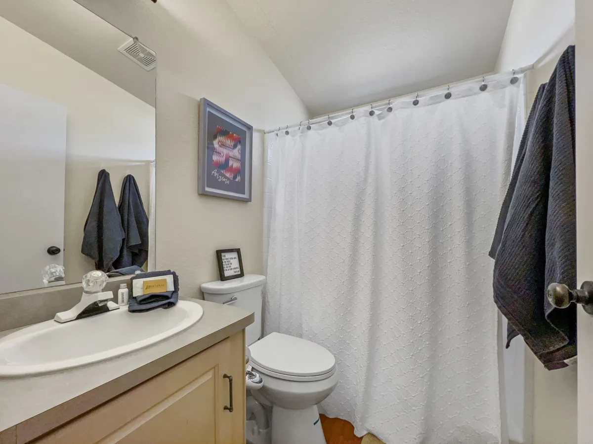 A well-appointed bathroom with a sink, toilet, shower curtain, and framed artwork. The space is clean and inviting, providing all essential amenities for comfort and convenience.
